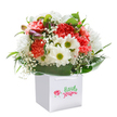 This striking bouquet, cradled in a pristine white gift bag with shimmering handles, radiates youthful delight and heartfelt energy, just like the welcoming spirit of Dartmouth Park itself. Layers of coral and peach carnations, each bloom soft and exquisitely ruffled, are gathered closely with crisp white daisies that feature bright, playful yellow-green centres-florals that seem to echo the lively mornings at neighbouring community cafes. Wisps of dainty baby's breath float among the fuller blossoms, their white tufts lending a sense of innocence and lightness. From the side, unopened purple-tipped buds peek through as though awaiting their moment, bringing dimensional intrigue and a touch of anticipation to the composition. Embracing the flowers, broad, dark green foliage forms a glossy natural wrap, securing the arrangement in a confident, rounded silhouette. The clean gift bag and pure white background make the colours sing without distraction-an ideal presentation for a thoughtful birthday surprise, a warm welcome to new neighbours, or simply a gesture meant to brighten a day. Each element is lovingly placed by your local Dartmouth Park Florist, drawing inspiration from the thriving streets and tranquil green corners of the area, ensuring every delivery carries a little of the neighbourhood's genuine warmth and vibrancy.